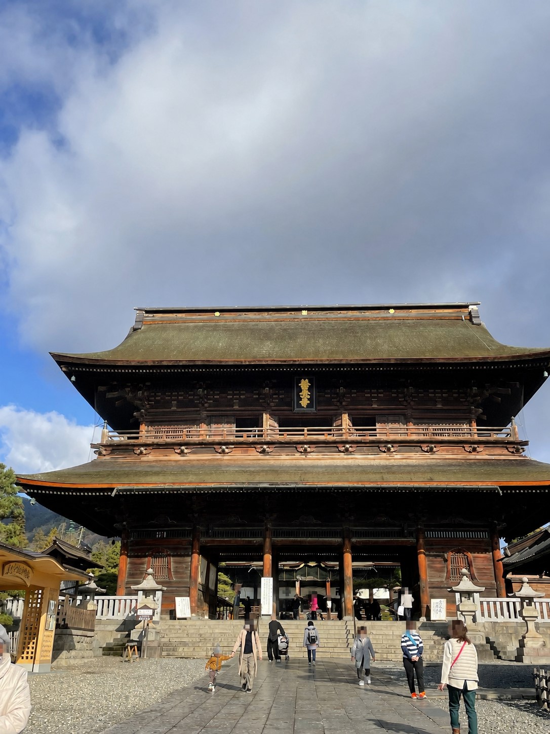 青空の下に立つ善光寺の山門と参拝者