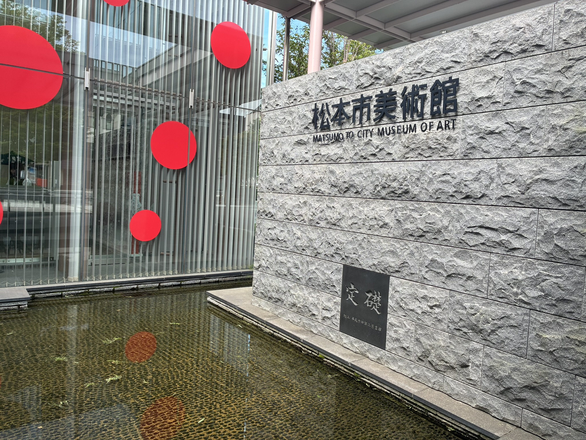 松本市美術館の定礎石碑と赤い水玉模様が見える建物